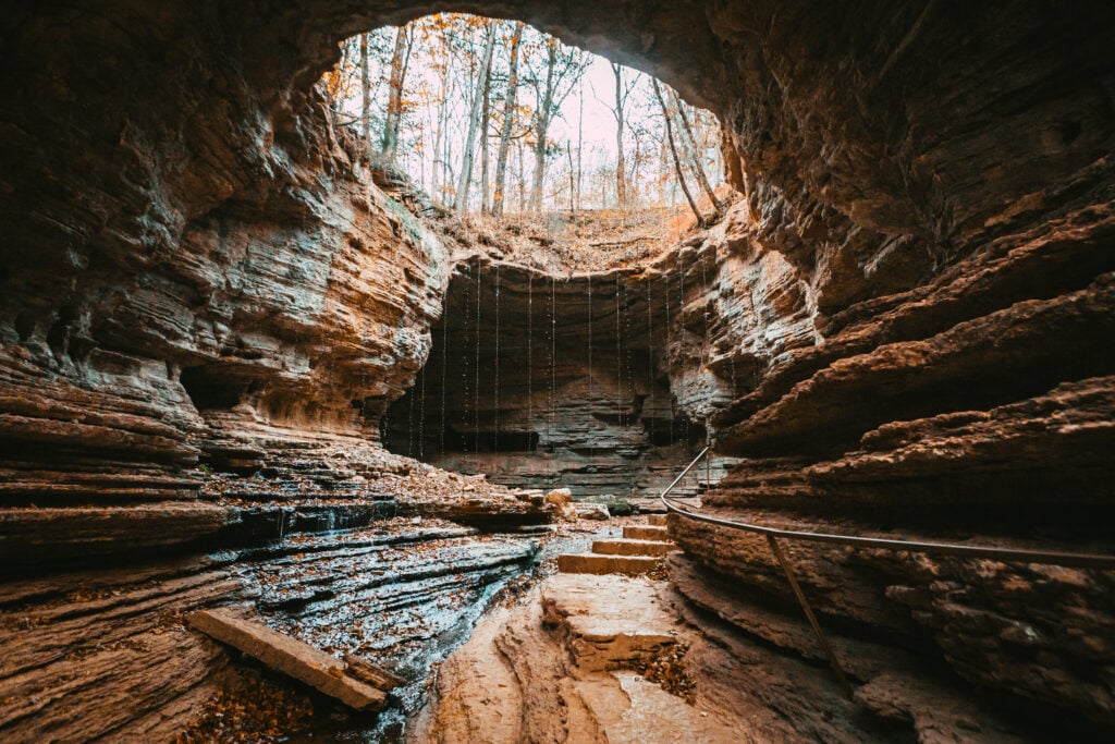 Natural rock bridge at The Bridges in Wayne County with layered stone walls, walking steps, railing, and wooded views above.